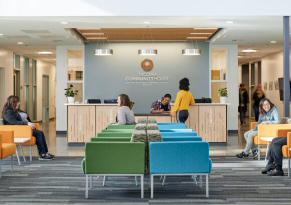 The main lobby of the Tacoma Community House building with colorful chairs and people sitting, standing, or talking.