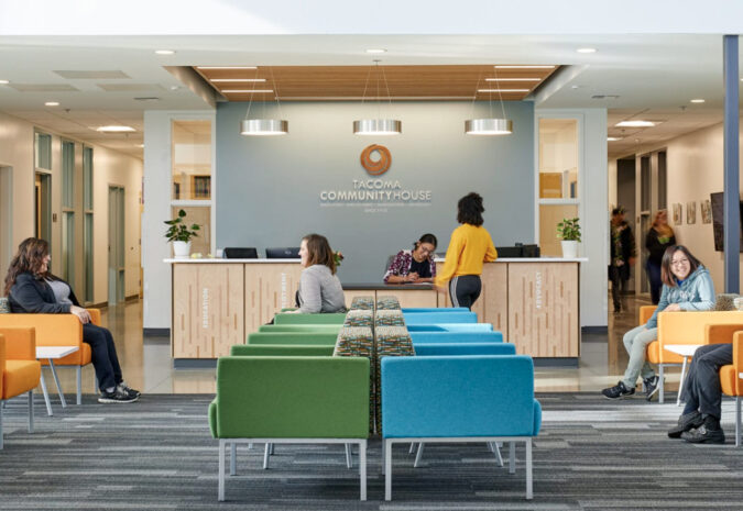 The main lobby of the Tacoma Community House building with colorful chairs and people sitting, standing, or talking.